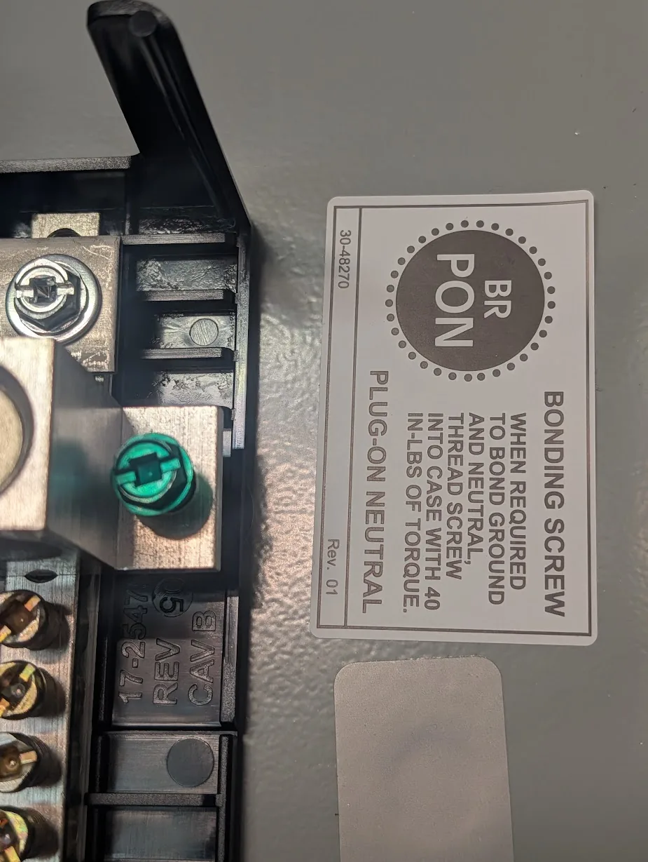 Close-up of the green bonding screw and the BR-style "bonding screw - when required" warning label